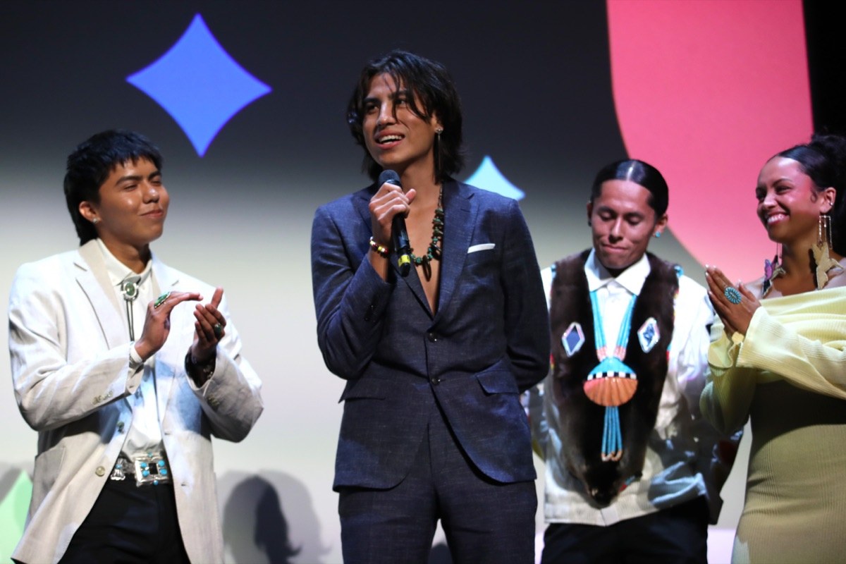 Kusem Goodwind speaking into a microphone on stage